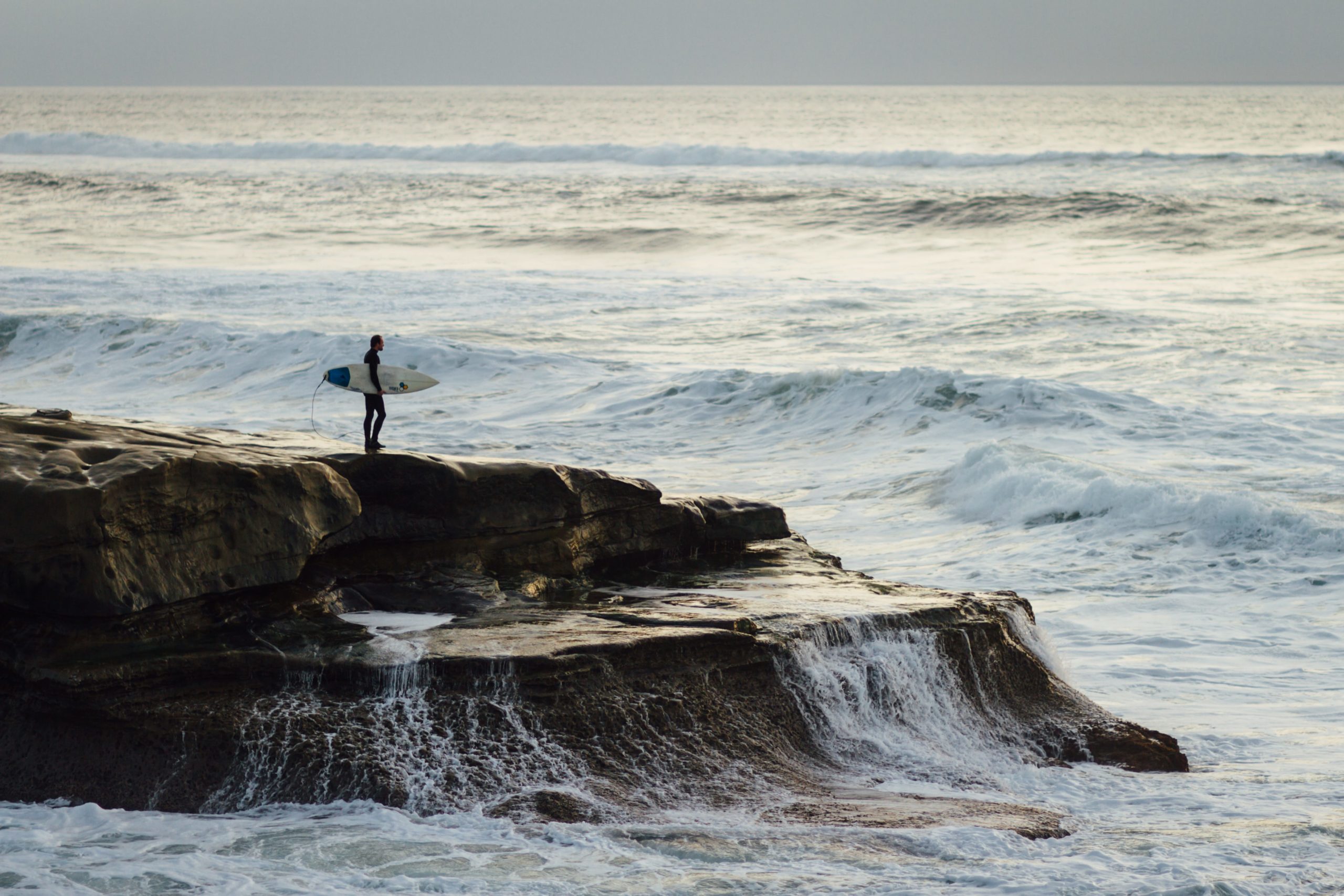 Ein Surfer plant von hohen Klippen ins Wasser zu springen, um ins Lineup zu gelangen. Sowohl die Energie der Wellen als auch der harte Meeresboden können in diesem Fall zu einer Surfverletzung führen.