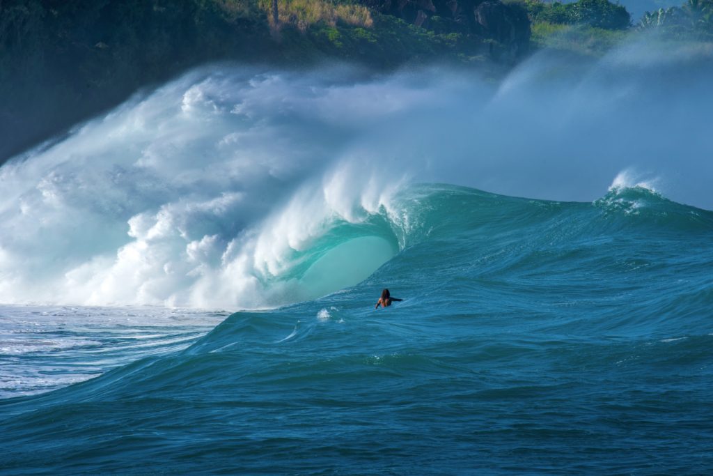 Ein Surfer sitzt bei riesigen Wellen im Lineup. Das Risiko für Verletzungen beim Surfen steigt in großen Wellen.